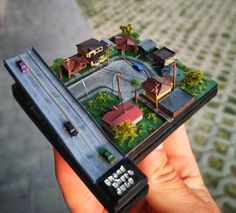 a person holding up a small model of a town with houses and trees on it