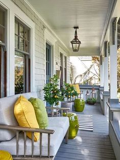 the front porch is decorated with white furniture and green pillows on it, along with potted plants