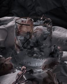 a glass filled with water sitting on top of a white cloth next to dead flowers