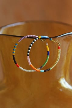 two bracelets with beads hanging from them on a wooden stand in front of a vase