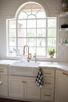 a kitchen with white cabinets and an arched window over the sink is pictured in this image