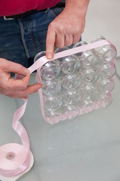 a person is holding a pink ribbon over an egg carton filled with empty wine glasses