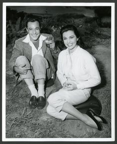 a man and woman are sitting on the ground drinking from wine glasses in an old black and white photo