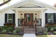 a white house with black shutters and plants on the front porch, along with steps leading up to it