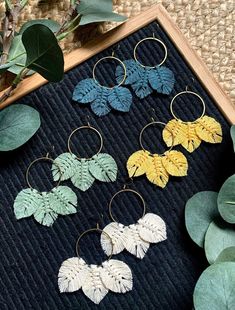 four pairs of earrings with leaves on them sitting next to some green plants and greenery