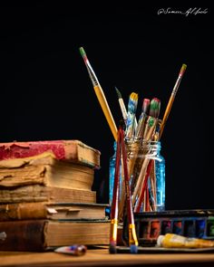 there are many pencils and paintbrushes in the jar on the table next to some books