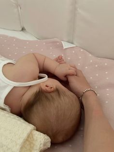 a baby laying on top of a bed next to a person's arm and hand