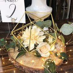 a white vase with flowers and greenery on a wooden table next to a sign that says save the date