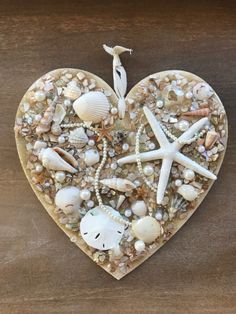 a heart shaped decoration with seashells and starfish in it on a wooden table