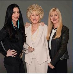 three women standing next to each other in front of a gray background with one woman holding her arm around the other