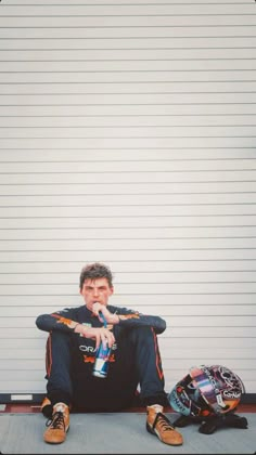 a man sitting on the ground next to his motorcycle helmet and drinking from a bottle