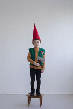 a young boy dressed in an elf costume standing on a small wooden stool holding a tool