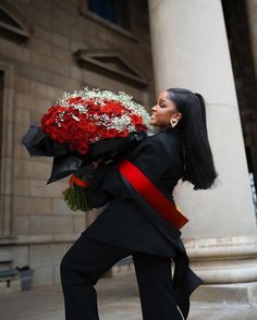 a woman in black jacket holding red and white flowers on her shoulder while standing next to columns