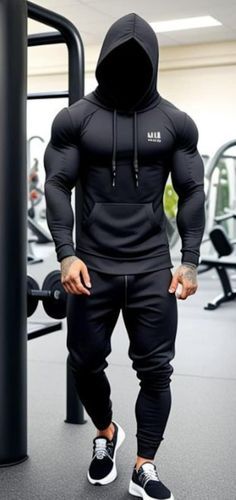 a man in black hoodie and sweatpants standing next to a gym equipment rack