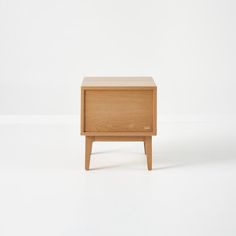 a small wooden nightstand sitting on top of a white floor next to an empty wall