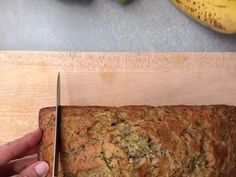 someone is cutting up a loaf of bread with a knife on a cutting board next to some bananas