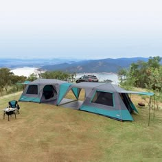 two tents are set up in the grass with mountains in the background, and one tent is empty