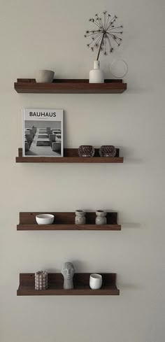 three wooden shelves with pictures, bowls and vases on them against a white wall