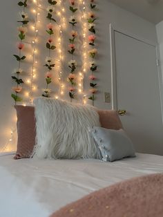 a white bed topped with lots of pillows and flowers next to a wall covered in lights