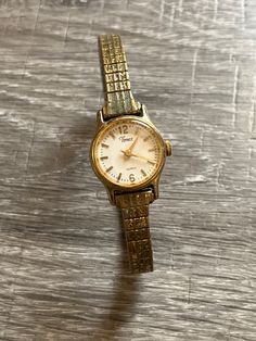 Vintage Women's Timex Quartz Watch. Adjustable stretch band.  Gold watch band, watch face is trimmed in gold with cream colored face and gold numbers numbers/time markings. Gold watch hands. There is some scratching on the face. Band is tarnished due to age. Unsure if it keeps time.  Engraved on back: Timex Base Metal Bezel Stainless Steel Back Water Resistant Philipines 377 BA Cell Gold Watch Band, Stretch Band, Stretch Bands, Watch Faces, Wrist Watches, Gold Earrings Studs, Gold Jewellery, Gold Studs, Base Metal