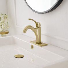 a bathroom sink with a gold faucet next to a mirror and flowers on the wall