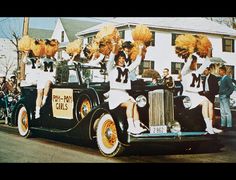 a group of people riding on the back of an old fashioned car with cheerleaders