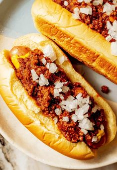 three hot dogs covered in cheese and chili on top of a wooden table next to each other