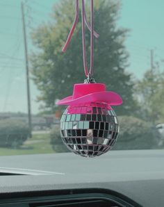 a disco ball ornament hanging from the dashboard of a car with pink ribbon