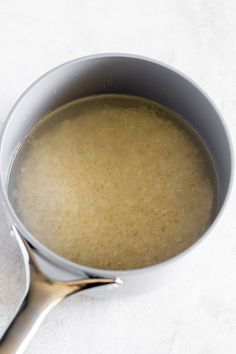 a silver pot filled with liquid on top of a white counter next to a spoon