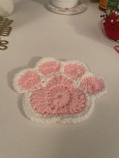 a pink and white crocheted dog paw on a table next to other items