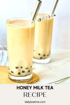 two glasses filled with honey milk tea on top of a wooden cutting board