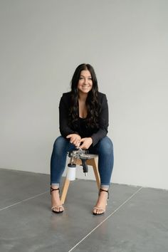 a woman sitting on top of a stool in front of a white wall with her legs crossed