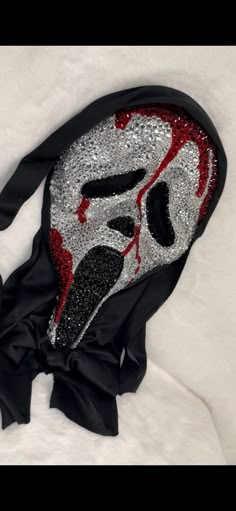 a black and red mask with silver sequins on it's face sitting on a white surface