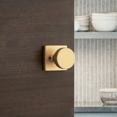 a door handle on a wooden cabinet with plates and bowls in the backround