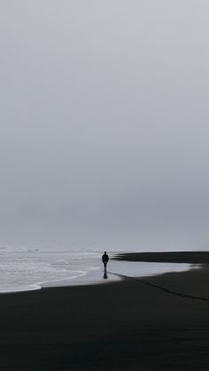 a lone person walking along the beach in front of the ocean on a gloomy day