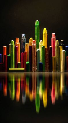 colorful crayons reflecting in the water on a black surface with reflections from them