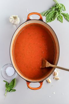 a pot filled with red sauce next to garlic and basil