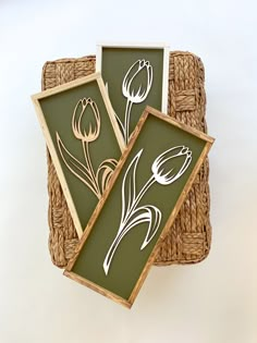 two framed pictures with flowers on them sitting on a wicker basket next to each other