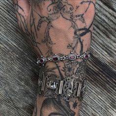 a man with tattoos on his arm and wrist is wearing a silver bracelet that has red stones