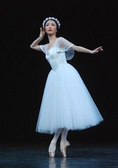 a woman in a white dress standing on a stage with her arms out to the side