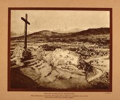 an old black and white photo of a cross on top of a hill with mountains in the background