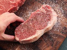 a person is cutting up raw meat on a wooden board with parmesan sprinkles