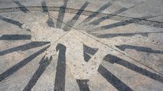 the sun is shining through some black and white lines on concrete floor with people walking in it