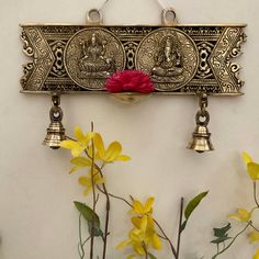 two bells hanging from the side of a wall with flowers in front of it and buddhas on them