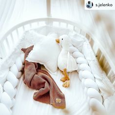 a stuffed duck laying on top of a white bed next to pillows and a blanket