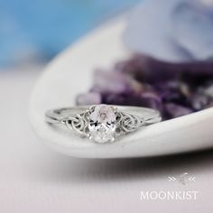 a close up of a ring on a white plate with purple flowers in the background