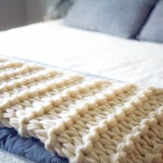 a white knitted blanket sitting on top of a blue and white bedspread