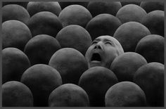 a man is surrounded by large balls in the shape of people's heads, with his eyes closed