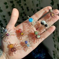 a person's hand with six different types of spider pins on it, all in various colors and sizes