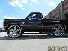 a black truck with chrome rims parked in a parking lot next to a building